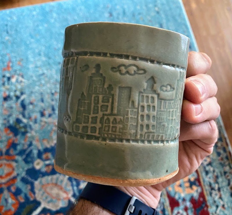 A gray clay mug with a cityscape design on it.