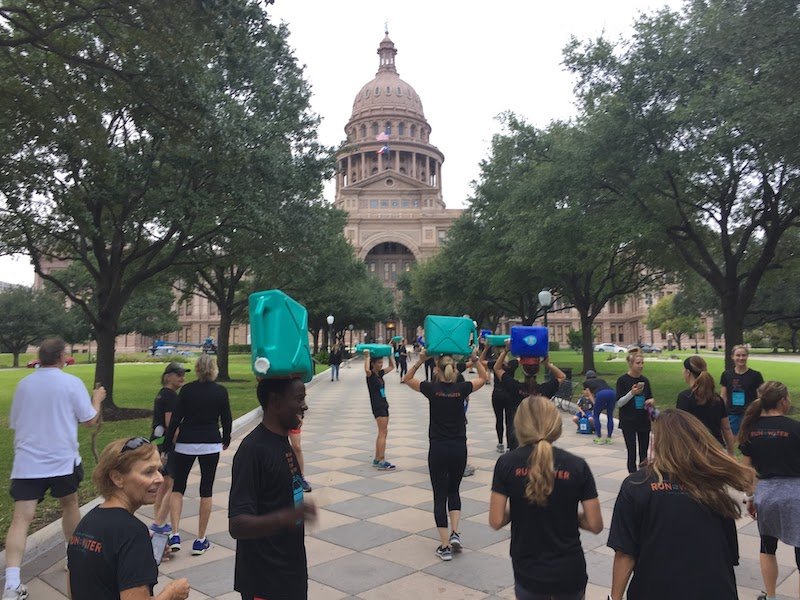 Several people outside the Austin state capital building with water jugs on their head in support of Run for the Water.